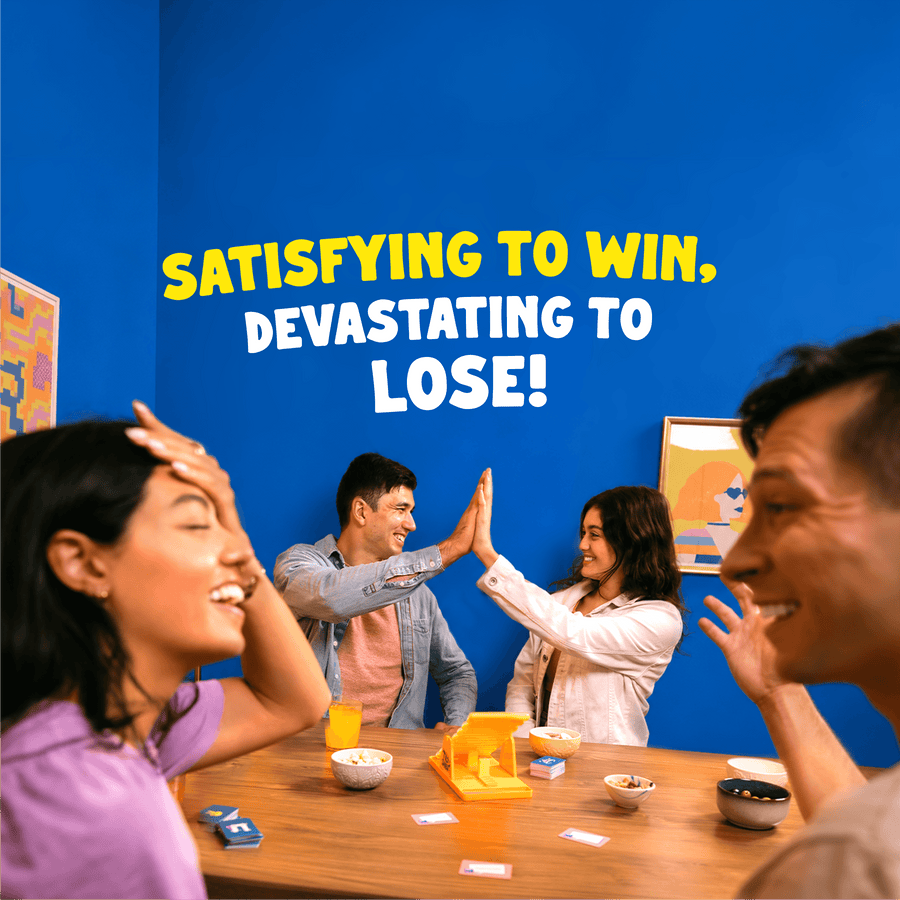 A group of four people laughing and high-fiving around a table in a brightly lit room with a vivid blue wall. Large text on the wall reads, 'SATISFYING TO WIN, DEVASTATING TO LOSE!' in white and yellow.